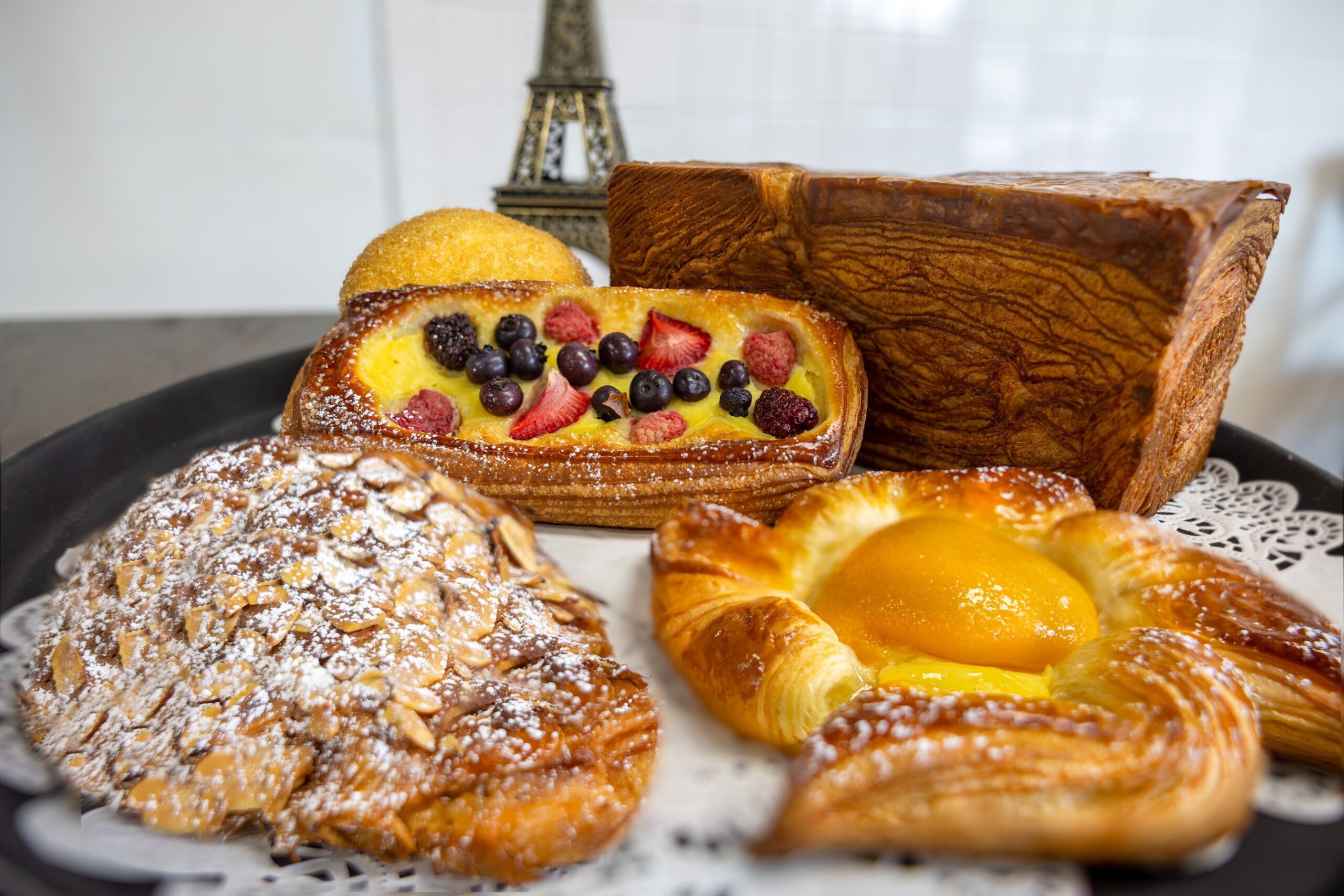 Assorted pastries on a serving tray: berry-filled loaf, almond pastry, and a glossy Danish bun.